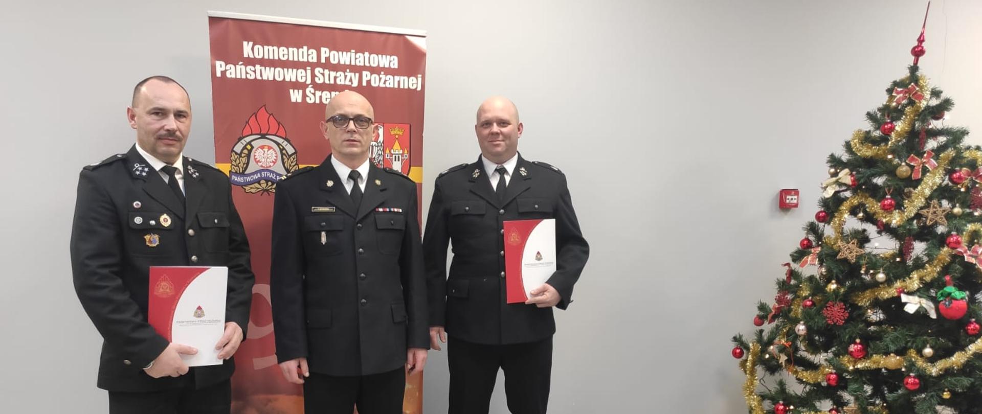 Na zdjęciu komendant powiatowy z prezesami OSP na tle baneru KP PSP Śrem z boku choinka 