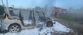 Na zdjęciu widać spalony samochód osobowy. Wokół samochodu widoczna jest piana gaśnicza. W tle widać samochody gaśniczev