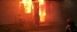 Widoczne płomienie w porze nocnej, strażak kucający przed wejściem do budynku