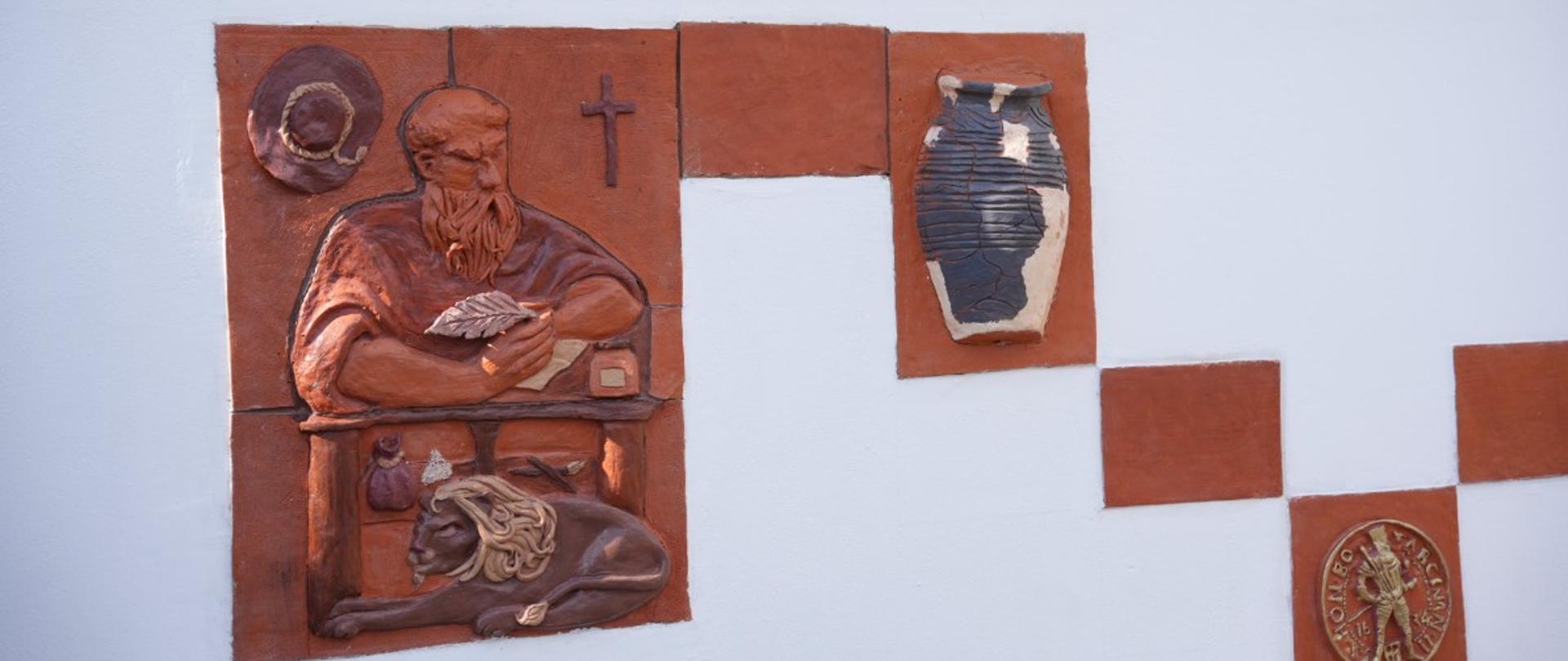 Ceramiczne płaskorzeźby ze św. Hieronimem i motywem dzbana zamontowane na murze 