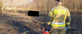 Pożar w miejscowości Chełmo. Na środku pogorzeliska ciało osoby która poniosła śmierć w pożarze trawy. Strażak ze zdjętym hełmem patrzy w kierunku gdzie znajduje się osoba poszkodowana.