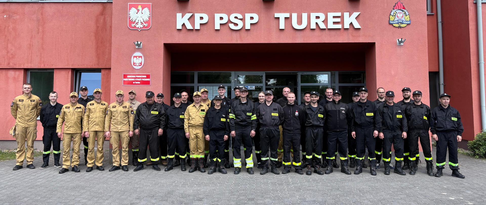 Grupa strażaków PSP i OSP pozuje do wspólnego zdjęcia przed budynkiem Komendy Powiatowej PSP w Turku.