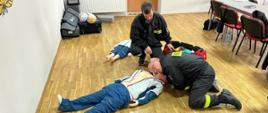 Kurs z zakresu kwalifikowanej pierwszej pomocy. Świetlica Komendy Powiatowej PSP w Rawiczu. Na podłodze leży "poszkodowany" fantom. Przy nim dwaj kursanci w ubraniach koszarowych "udzielający KPP" Jeden z nich sprawdza oddech.