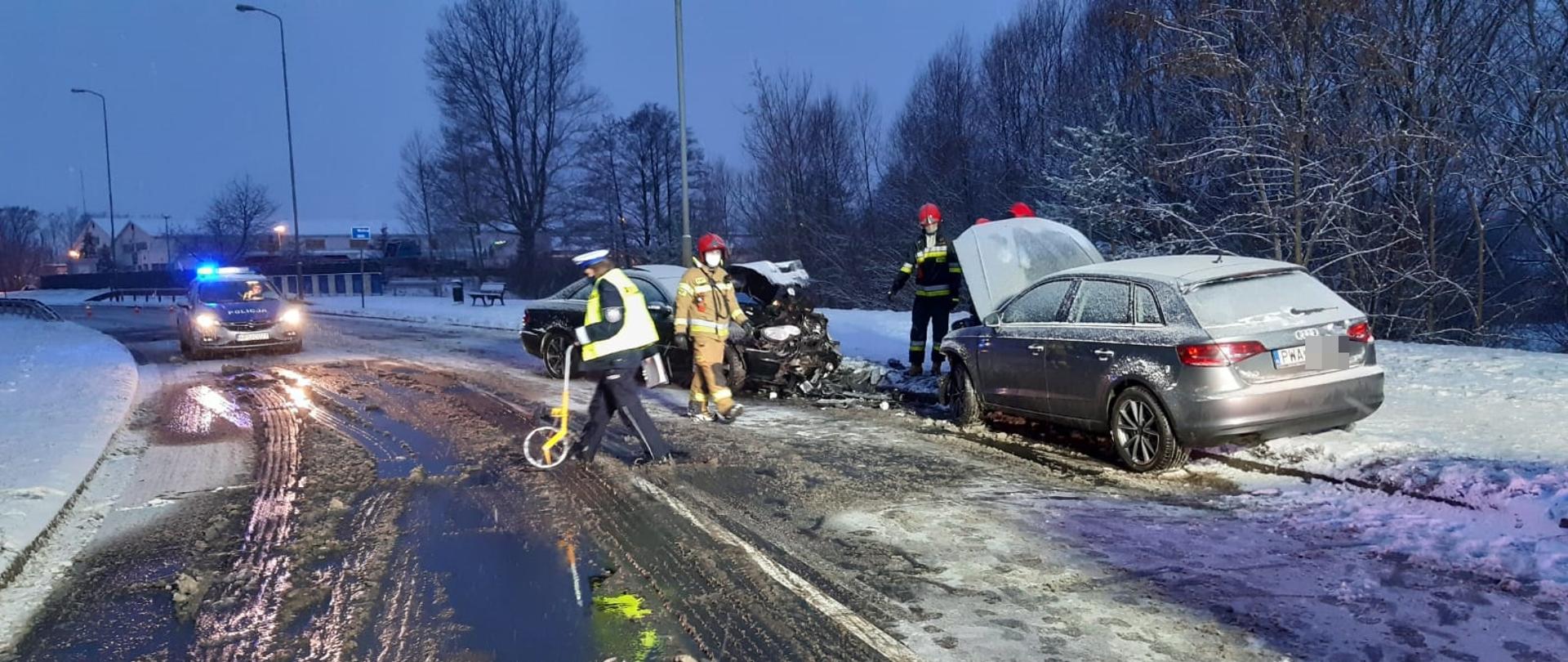 Na zdjęciu widać rozbite pojazdy oraz strażaków i policjantów, a w tle radiowóz policyjny 