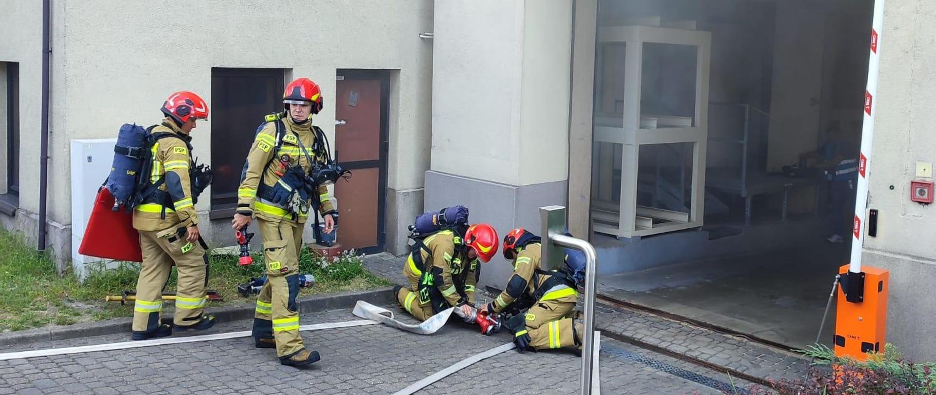 Na zdjęciu znajdują się strażacy prowadzący działania ratowniczo- gaśnicze. Na zdjęciu widać wydobywające się zadymienie.