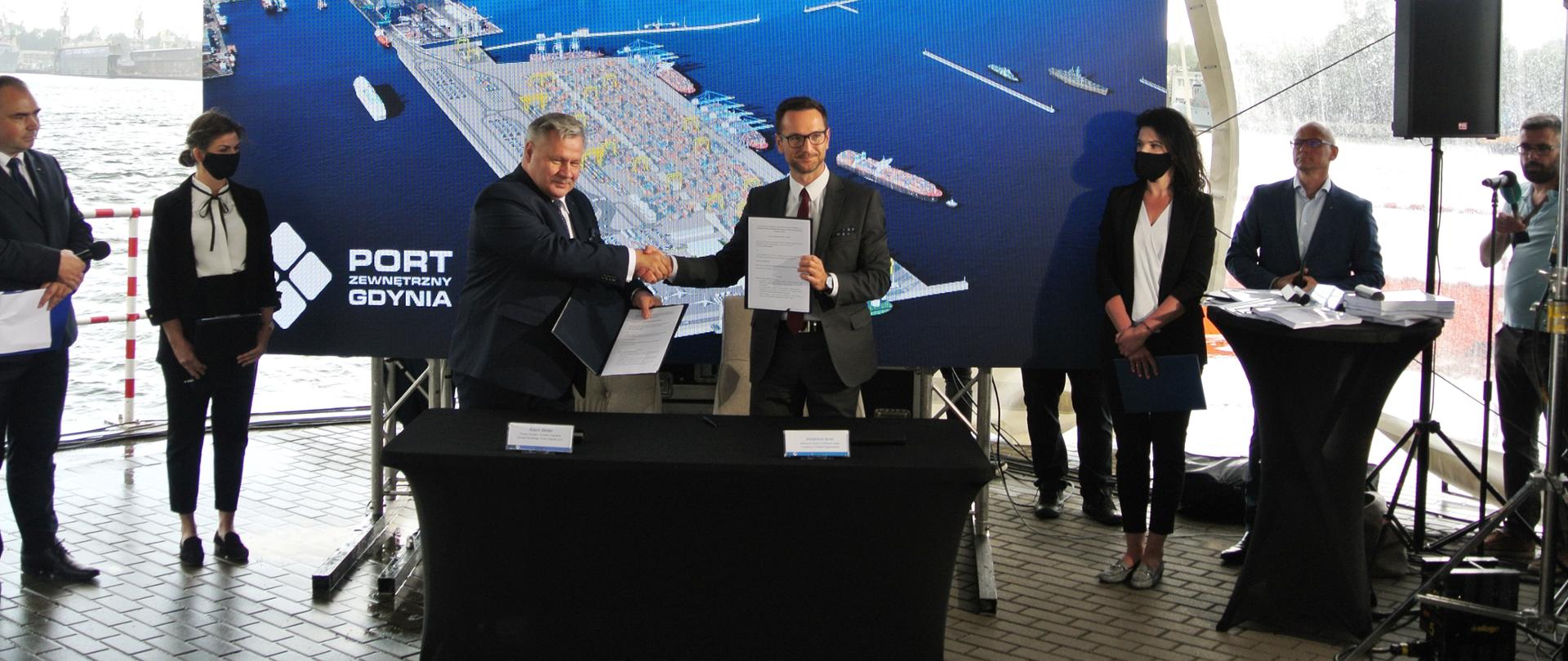 Dwóch mężczyzn podaje sobie ręce i wymienia się podpisanymi dokumentami