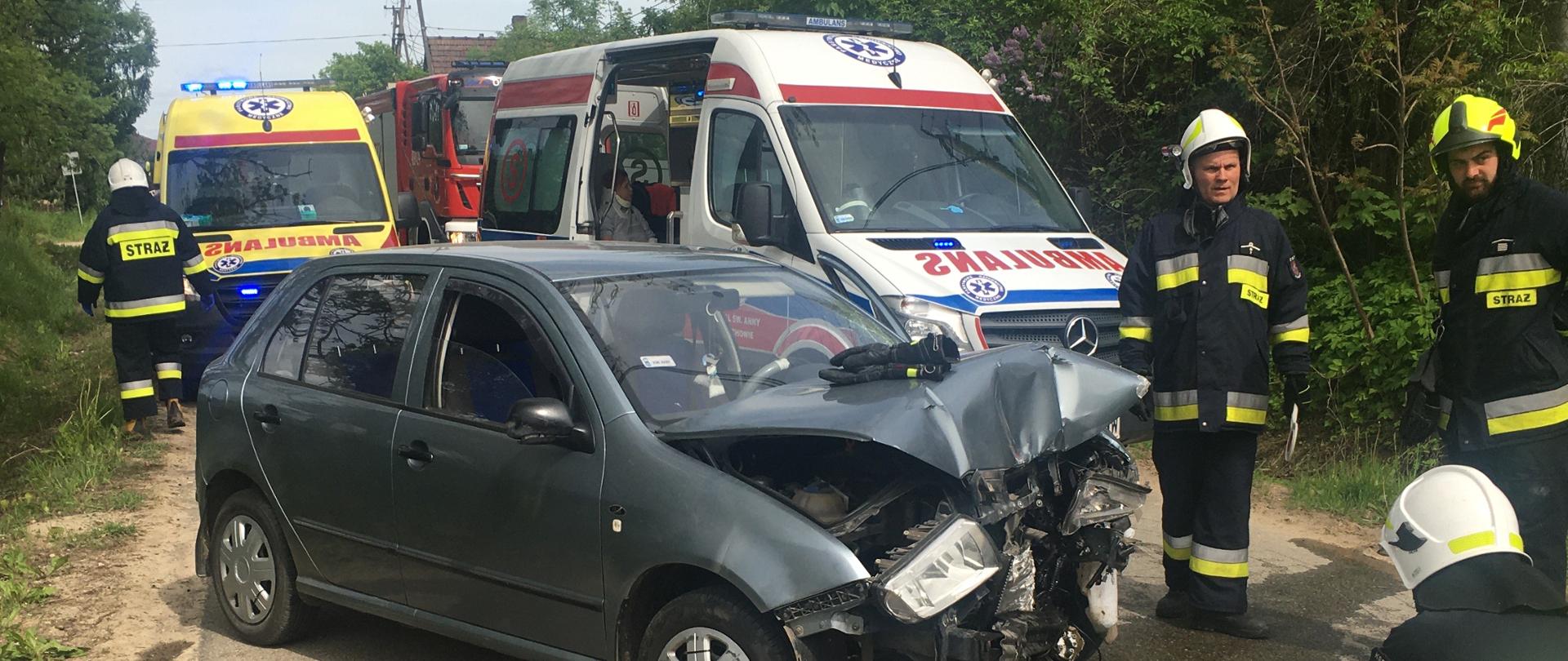 Alt. na miejscu widoczne jest jeden samochód PSP, oraz dwie kratki Zespołów Ratownictwa Medycznego w której ratownicy medyczni zabezpieczaj osobę poszkodowaną oraz samochód osobowy ,który znajduje się na jezdni z widocznymi uszkodzeniami karoserii przy nim trzech strażaków OSP