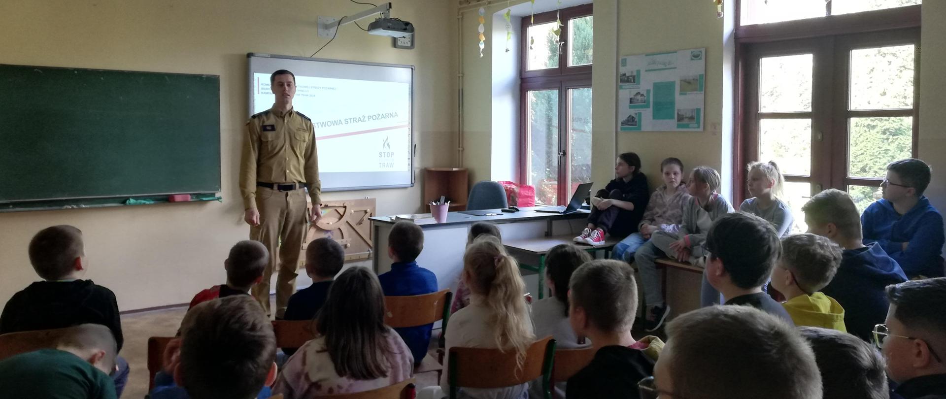 Funkcjonariusz w klasie przedstawia dla dzieci prezentacje „STOP POŻAROM TRAW”