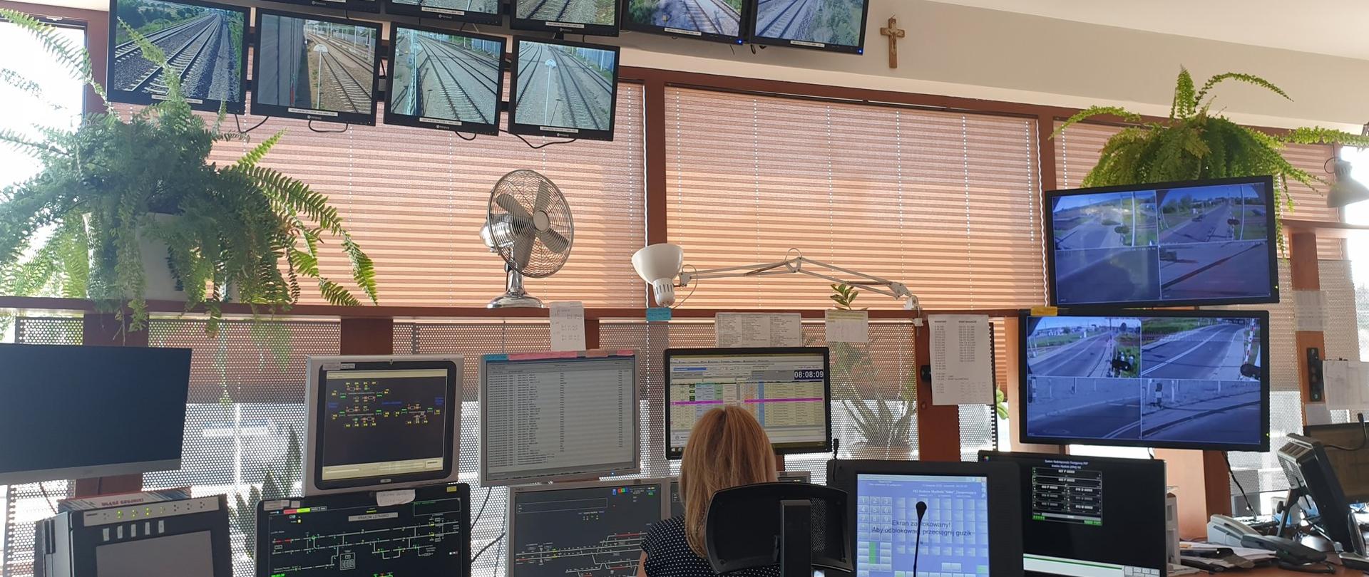 Na zdjęciu widać wnętrze Lokalnego Centrum Sterowania. Przed monitorami siedzi kobieta, a przed nią znajdują się monitory do sterowania ruchem kolejowym. 