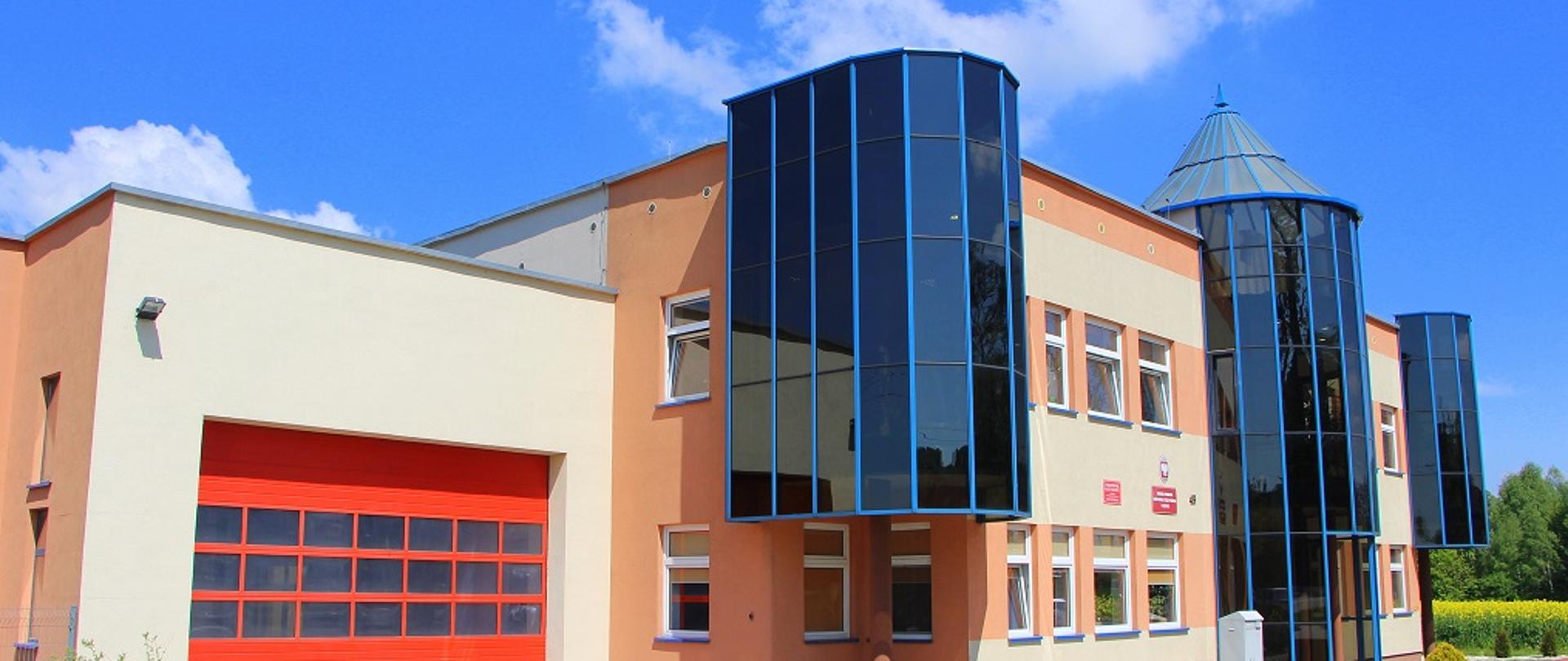 obiekt komendy powiatowej w Złotoryi, po lewej stronie czerwona brama garażowa, nad obiektem bezchmurne niebo