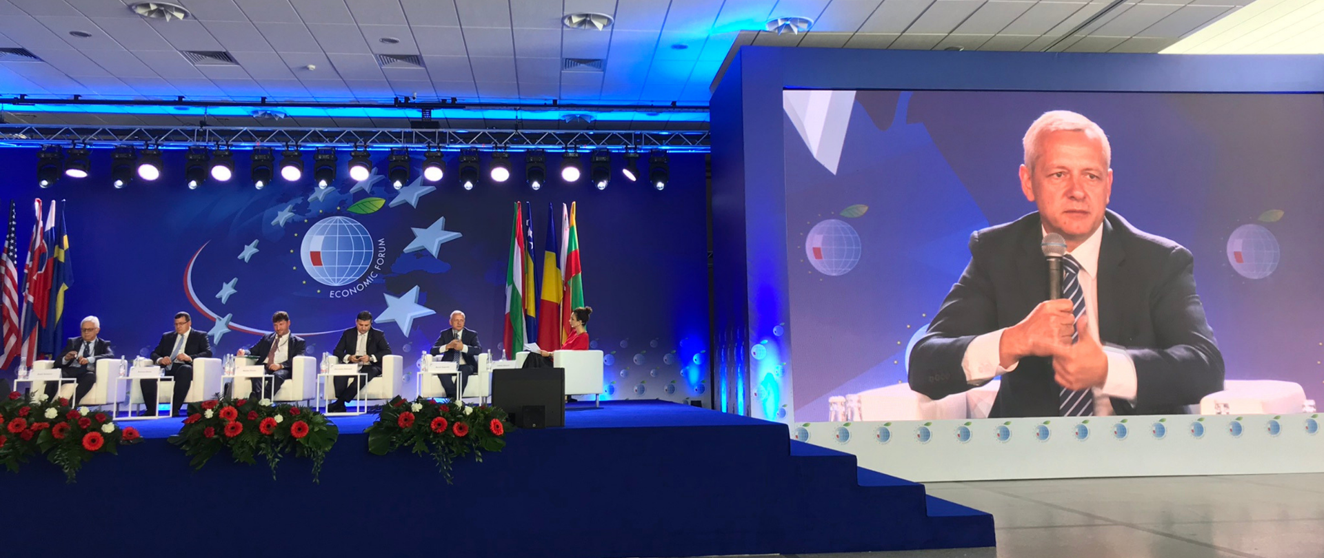 Sala konferencyjna. Na scenie siedzą uczestnicy panelu. Po prawej stronie telebim, na który widać w zbliżeniu ministra cyfryzacji Marka Zagórskiego