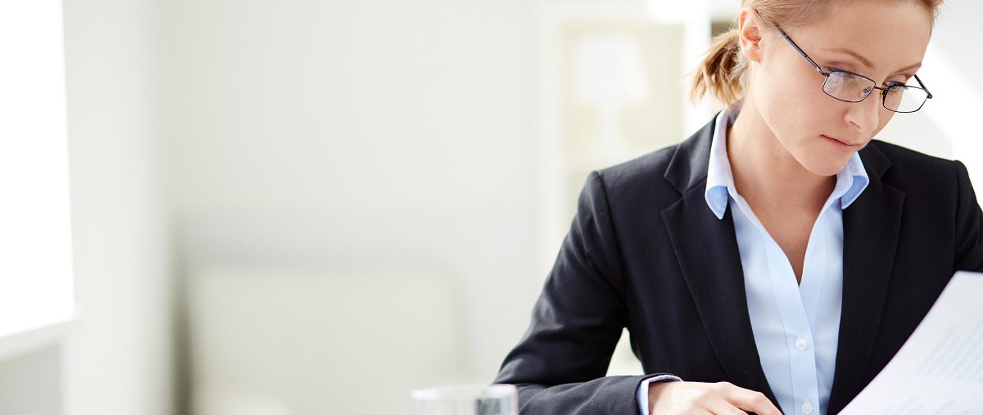 Młoda przedsiębiorczyni siedzi w miejscu pracy i czyta dokumenty leżące na stole