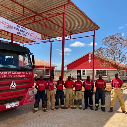 Wóz strażacki i pozujący do zdjęcia czarnoskórzy strażacy.