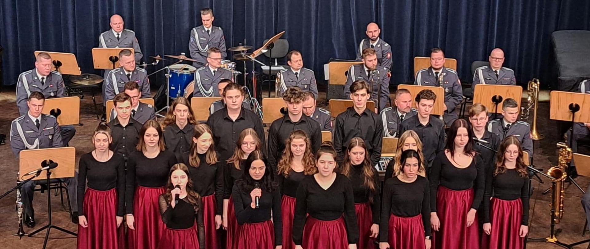 Zdjęcie przedstawiające występ uczniów szkoły, którym akompaniuje orkiestra wojskowa. Impreza: wręczenie nagród laureatom konkursu "Żołnierze Wyklęci. Niezłomni Bohaterowie"