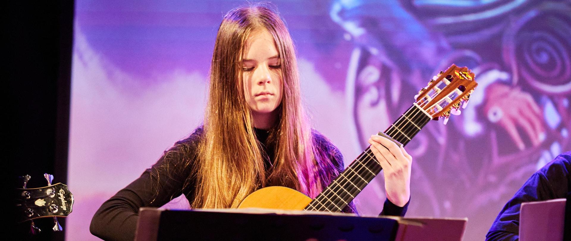 Uczennica gra na gitarze, na zdjęciu statyw