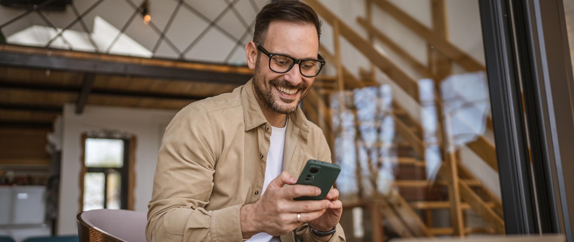 Uśmiechnięty mężczyzna w okularach z telefonem w rękach