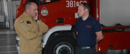 Wizyta strażaków z Attendorn. Garaż w komendzie w Lesznie. Jeden z leszczyńskich strażaków, na tle wozu pożarniczego opowiada jednemu z gości o jednostce, w której pełni służbę. 