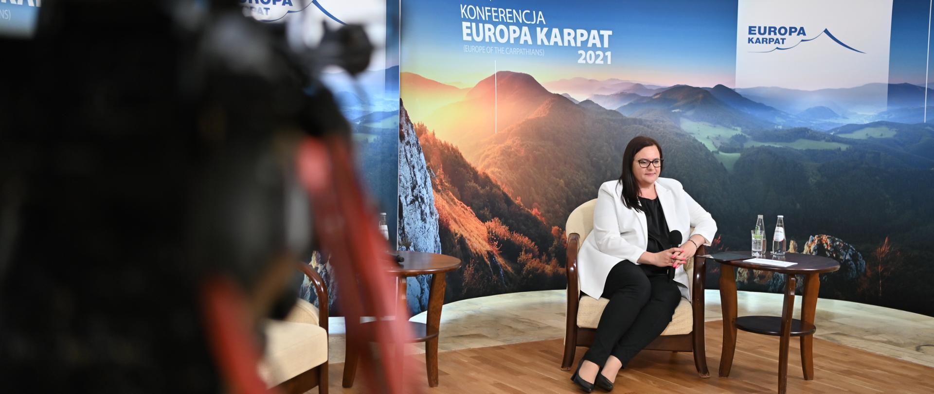 Na zdjęciu wiceminister funduszy i polityki regionalnej Małgorzata Jarosińska-Jedynak siedząca przy stoliku w trakcie konferencji. W tle ścianka Konferencji Europa Karpat.