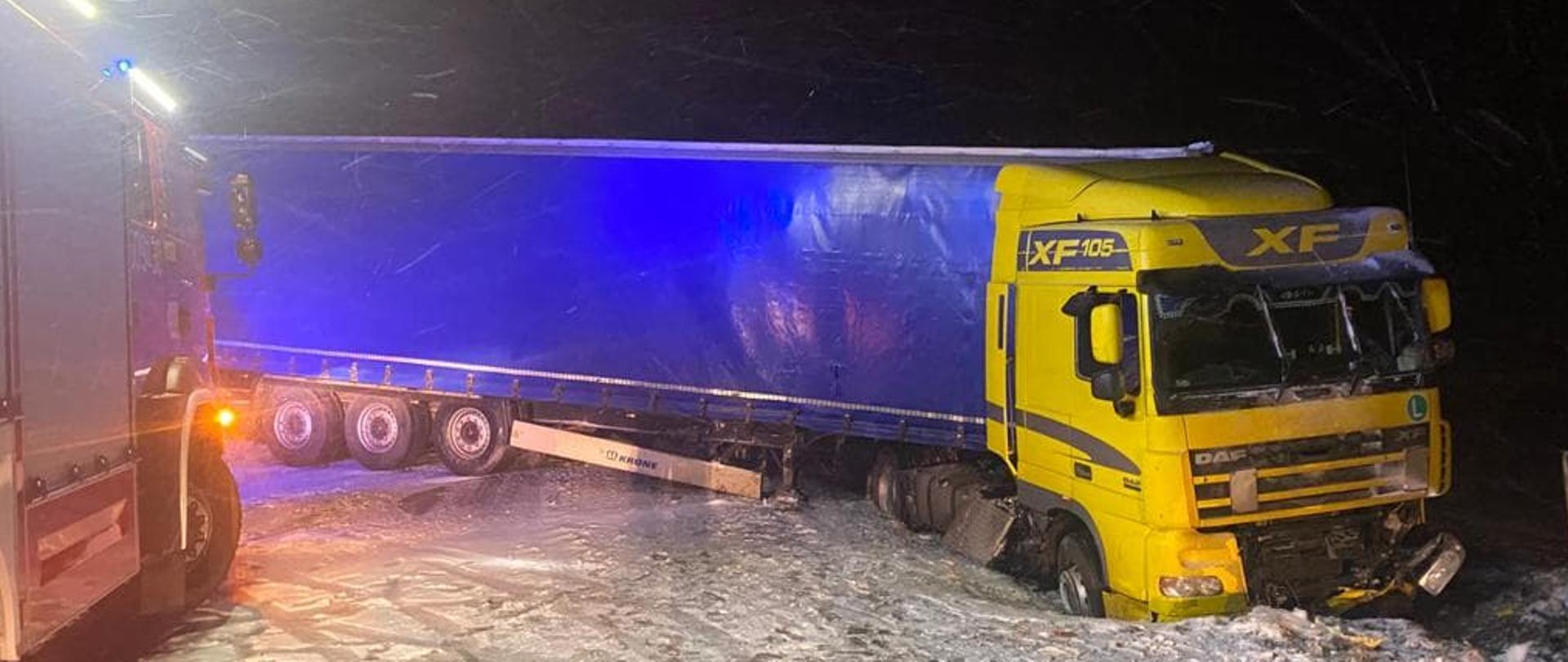 Samochód ciężarowy znajduje się częściowo w rowie blokując drogę. 