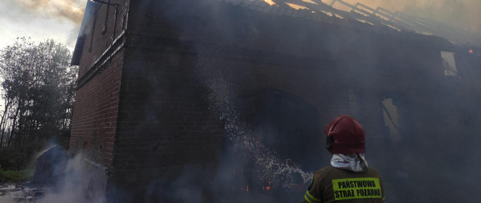 Zdjęcie przedstawia strażaka gaszącego zagrożony obiekt