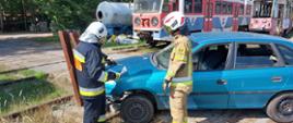 Dwóch druhów ochotniczych straży pożarnych podczas zajęć kierującego działaniem ratowniczym dla strażaka- ratownika OSP. Dowodzący akcją wskazuje miejsce cięcia na samochodzie drugiemu druhowi. 