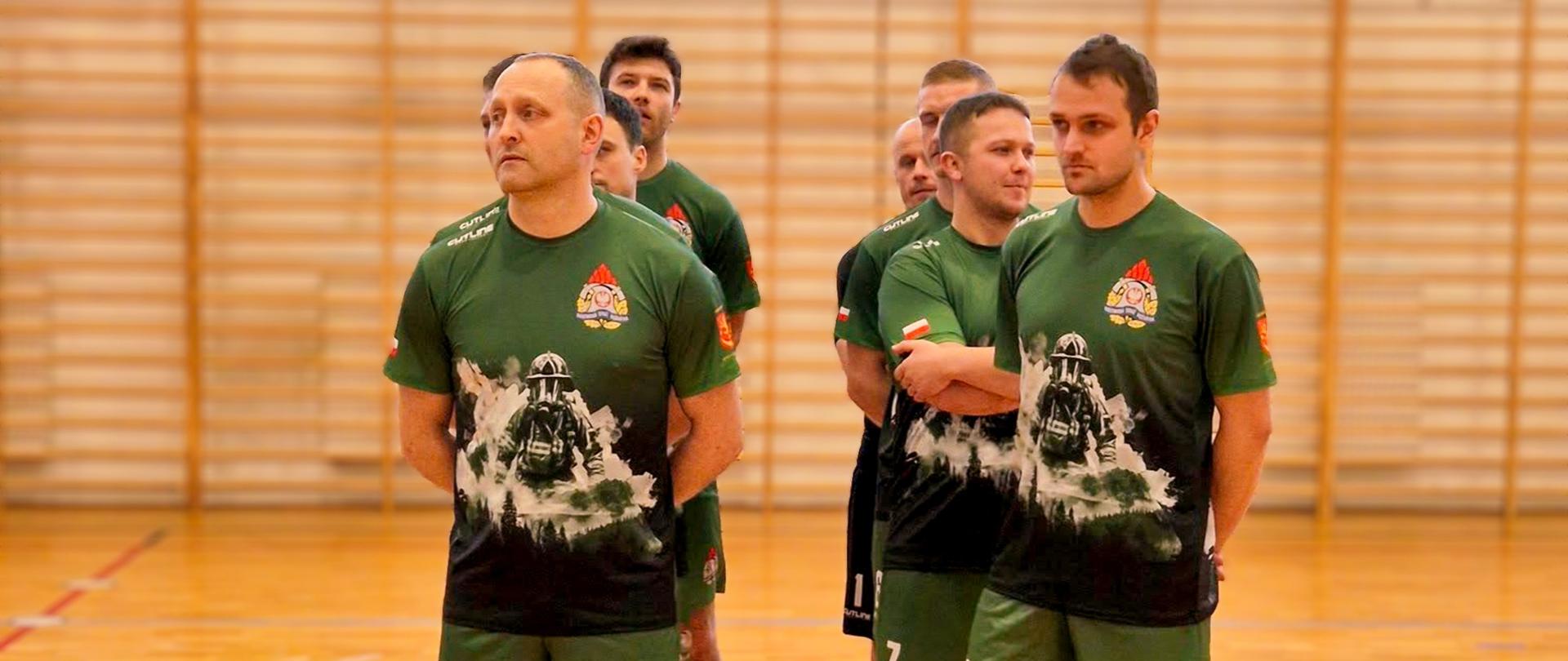 Zdjęcie przedstawia drużynę z KP PSP w Ustrzykach Dolnych w futsalu. Zawodnicy stoją w strojach sportowych na hali sportowej. 