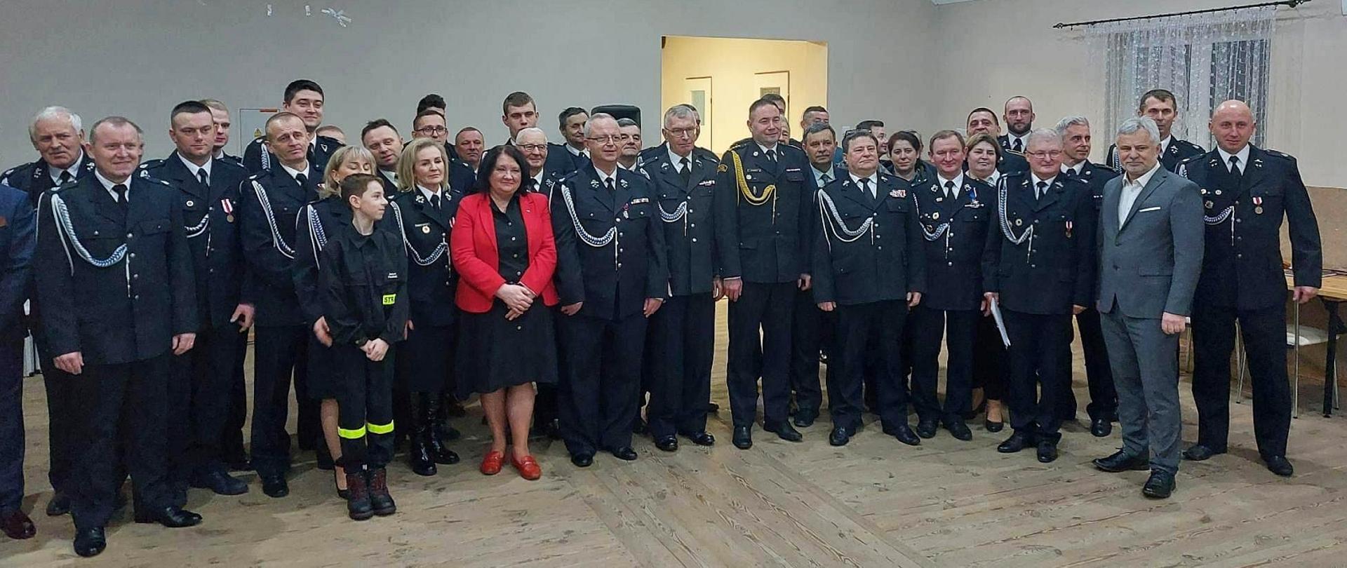 druhowie, strażacy oraz oficjale pozujący do zdjęcia grupowe w sali 