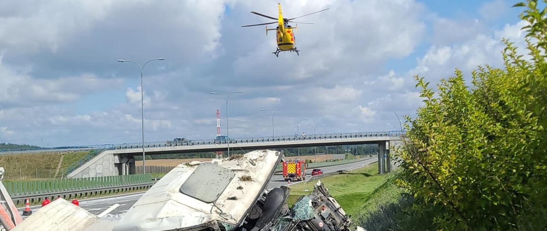 Wrak ciężarówki na skarpie przy autostradzie, w tle odlatujący śmigłowiec LPR