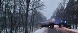 Zdjęcie przedstawia ciągnik rolniczy wraz z cysterną ustawiony w poprzek drogi.