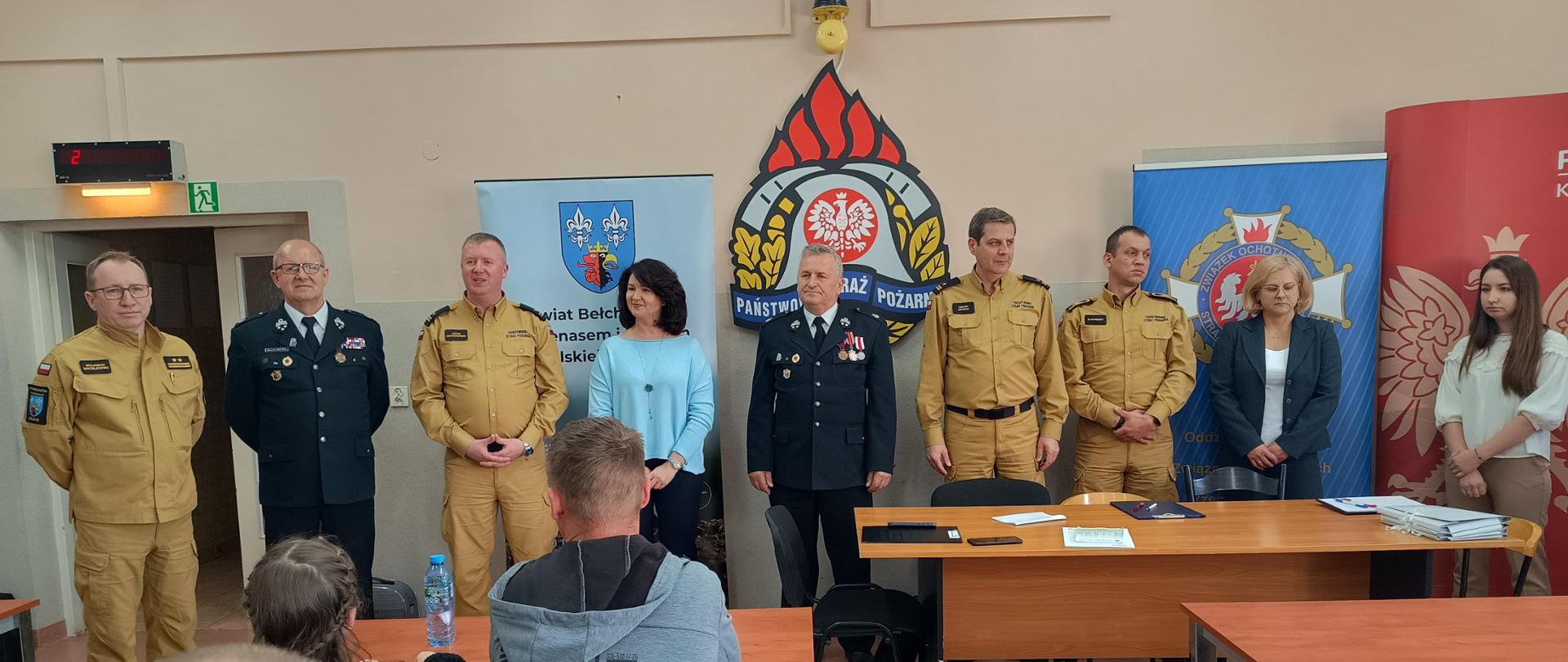 na zdjęciu strażacy w mundurach służbowych oraz zaproszeni goście podczas otwarcia ogólnopolskiego turnieju wiedzy pożarniczej w tle banery powiatu, straży pożarnej oraz OSP