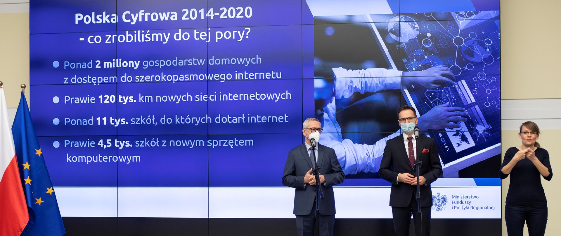 Ministrowie Marek Zagórski i Waldemar Buda podczas konferencji prasowej - stoją przed mikrofonami, z ich lewej strony - tłumaczka migowa. Na nimi ekran prezentacji z treścią: Polska Cyfrowa 2014-2020 - co rozbiliśmy do tej pory?