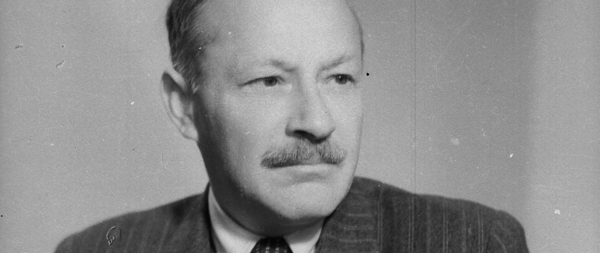 Zygmunt Modzelewski - portret mężczyzny z wąsem, ciemne włosy, ciemna marynarka w paski, ciemny krawat w drobne wzorki, biała koszula.