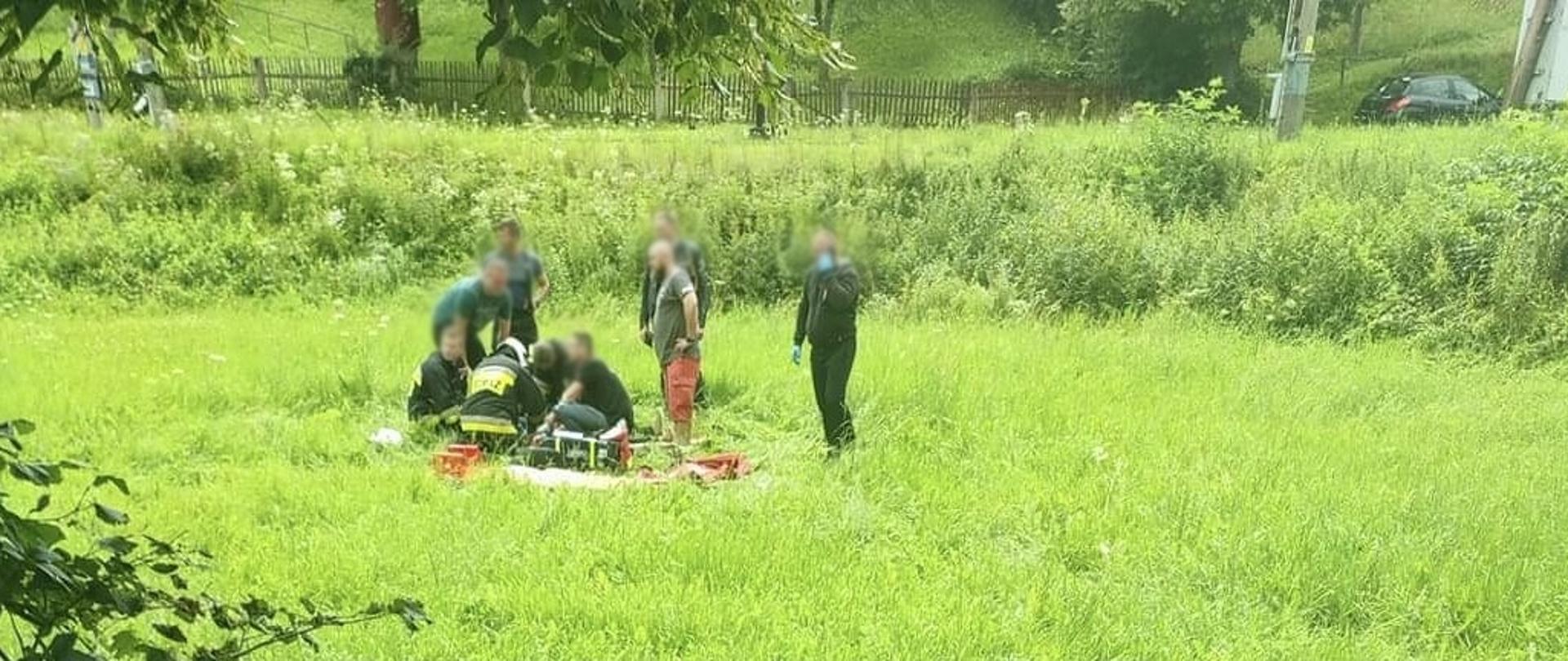 Osoby udzielające pomocy osobie poszkodowanej na trawie