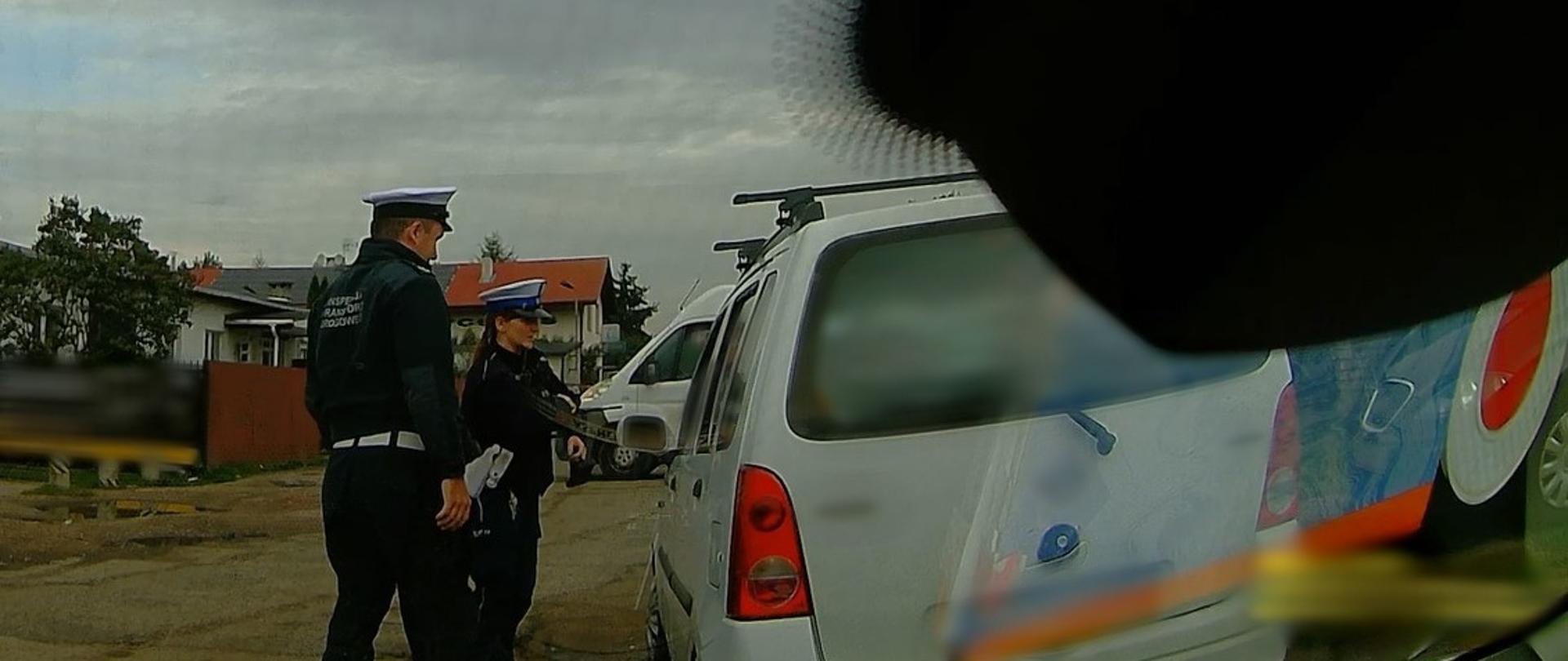 Obraz z wideo-rejestratora zamontowanego za przednią szybą nieoznakowanego radiowozu ITD: umundurowany inspektor Inspekcji Transportu Drogowego i funkcjonariusz Policji stoją obok zatrzymanego do kontroli samochodu osobowego i rozmawiają z kierującym.