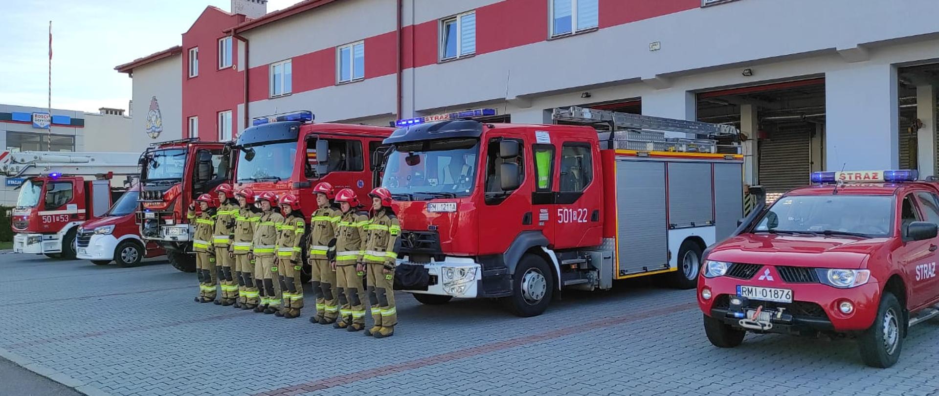 Na fotografii strażacy ubrani w ubrania bojowe stoją w postawie zasadniczej przed pojazdami pożarniczymi oddając hołd poległym w katastrofie smoleńskiej w jej 12 rocznicę. Fotografia wykonana przed budynkiem jednostki ratowniczo-gaśniczej nr 1 w Mielcu.