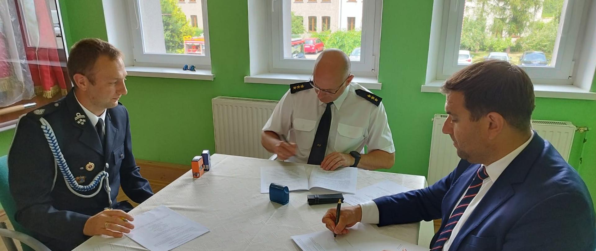 Obraz przedstawia Komendanta Powiatowego, Prezes OSP i Burmistrza podczas podpisywania porozumienia
