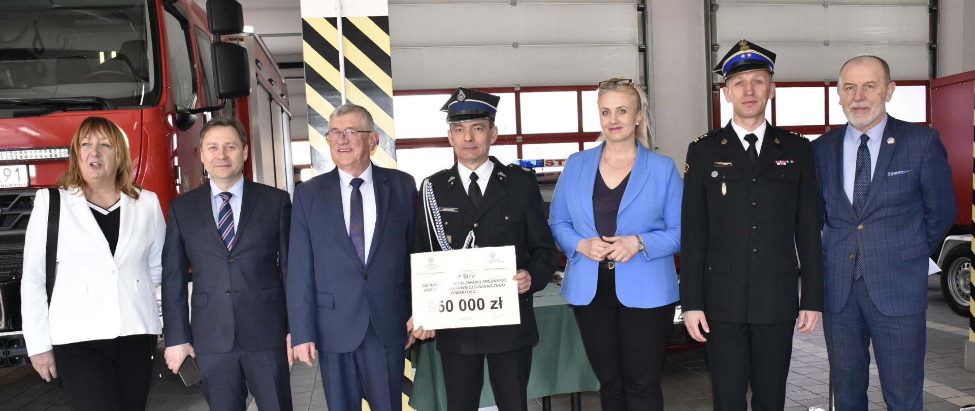 zdjęcie grupowe ,garaż , osoby cywilne oraz strażacy stoją przed samochodem strażackim