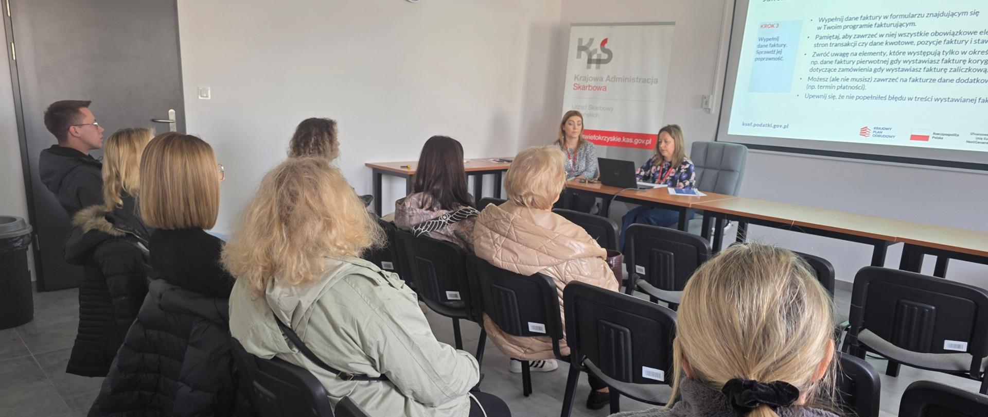 W sali siedzi grupa osób i słucha wykładu o Krajowym Systemie e-Faktur
