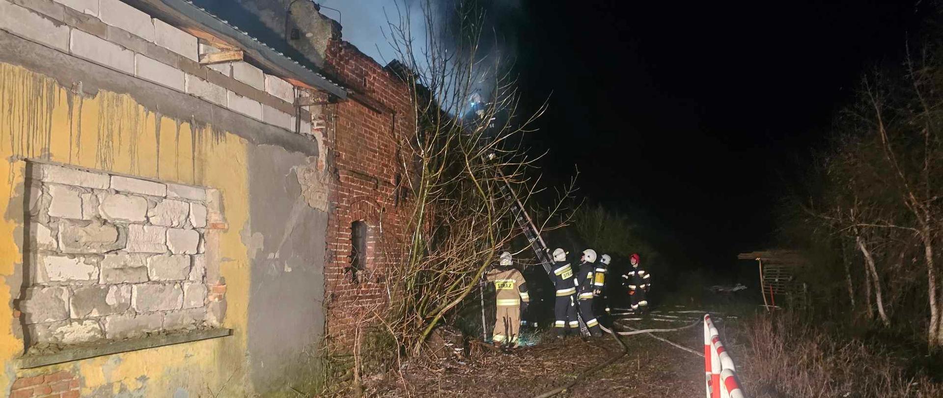 Strażacy zabezpieczają drabinę przystawioną do budynku gospodarczego. Na drabinie stoi strażak.