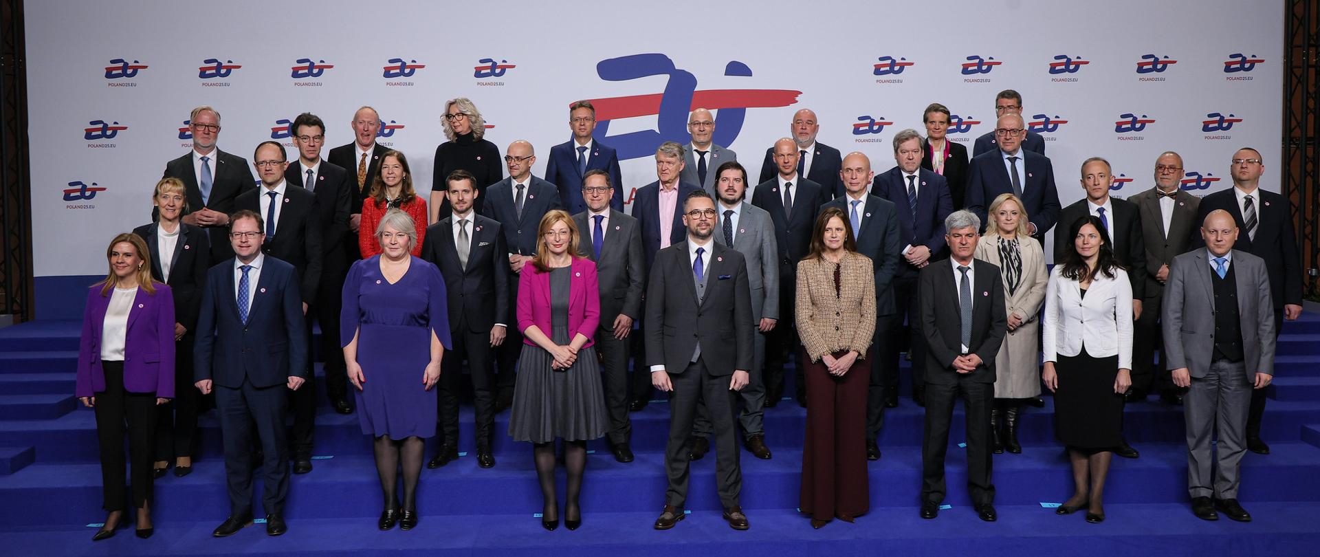 Zdjęcie zbiorowe, na niebieskiej podłodze pod ścianą z wielkim logo Prezydencji stoi grupa kilkudziesięciu osób, pośrodku grupy minister Kulasek.