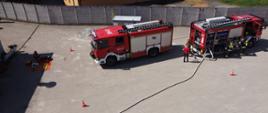 widok z góry na plac przed zakładem. Na środku 2 wozy strażackie, obok strażacy w piaskowych mundurach i rozwinięta linia gaśnicza