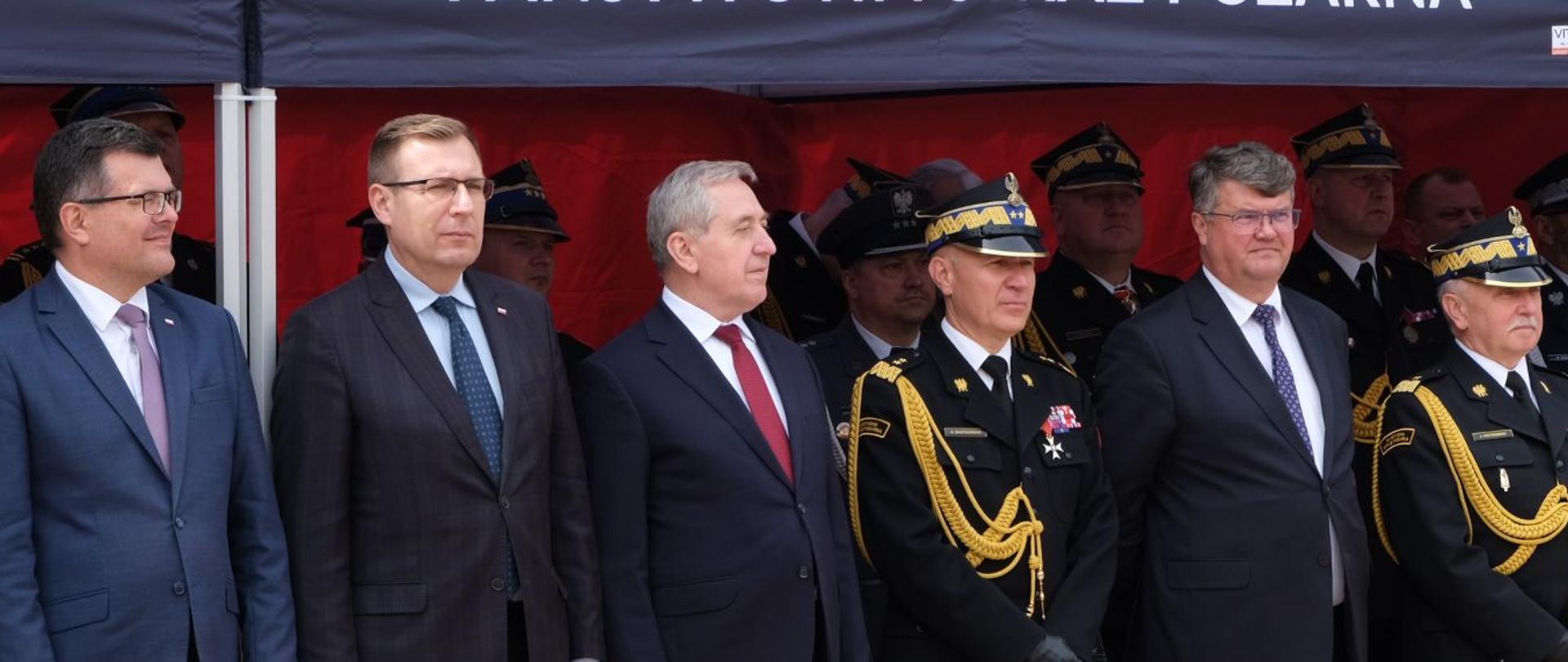 grupa mężczyzn i strażaków stoi pod namiotemv z napisem państwowa straż pożarna