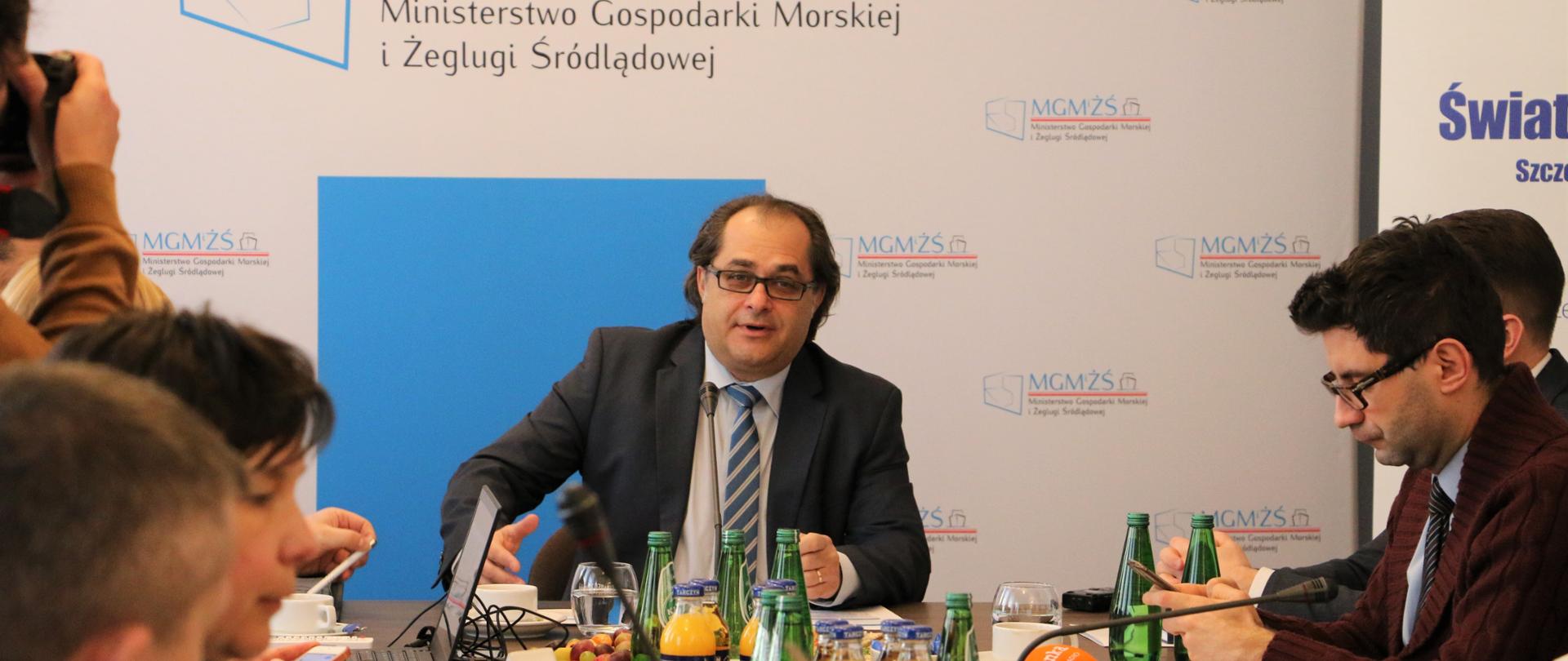 W centrum zdjęcia znajduje się minister Marek Gróbarczyk, który przemawia do zebranych dziennikarzy.