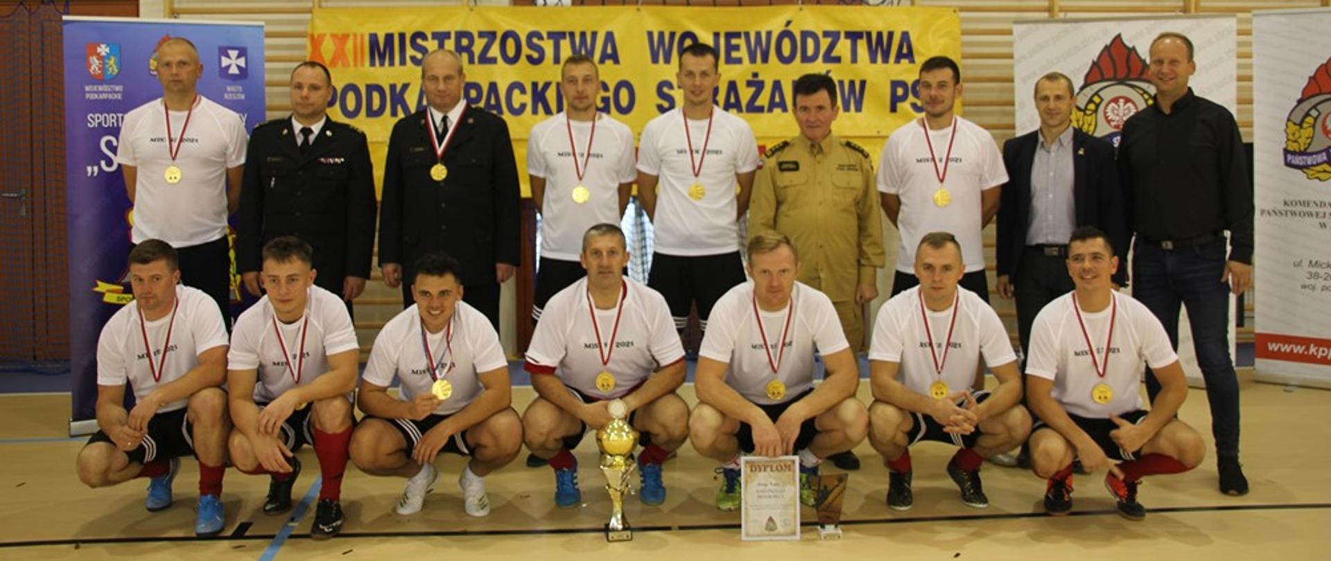 Na zdjęciu widzimy zwycięzców turnieju w piłce halowej, w raz z komendantami pozującymi z medalami i pucharem do grupowego zdjęcia na tle banneru zawodów.