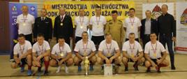 Na zdjęciu widzimy zwycięzców turnieju w piłce halowej, w raz z komendantami pozującymi z medalami i pucharem do grupowego zdjęcia na tle banneru zawodów.