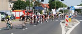 peleton kolarzy jedzie drogą, w tle widać samochód pożarniczy