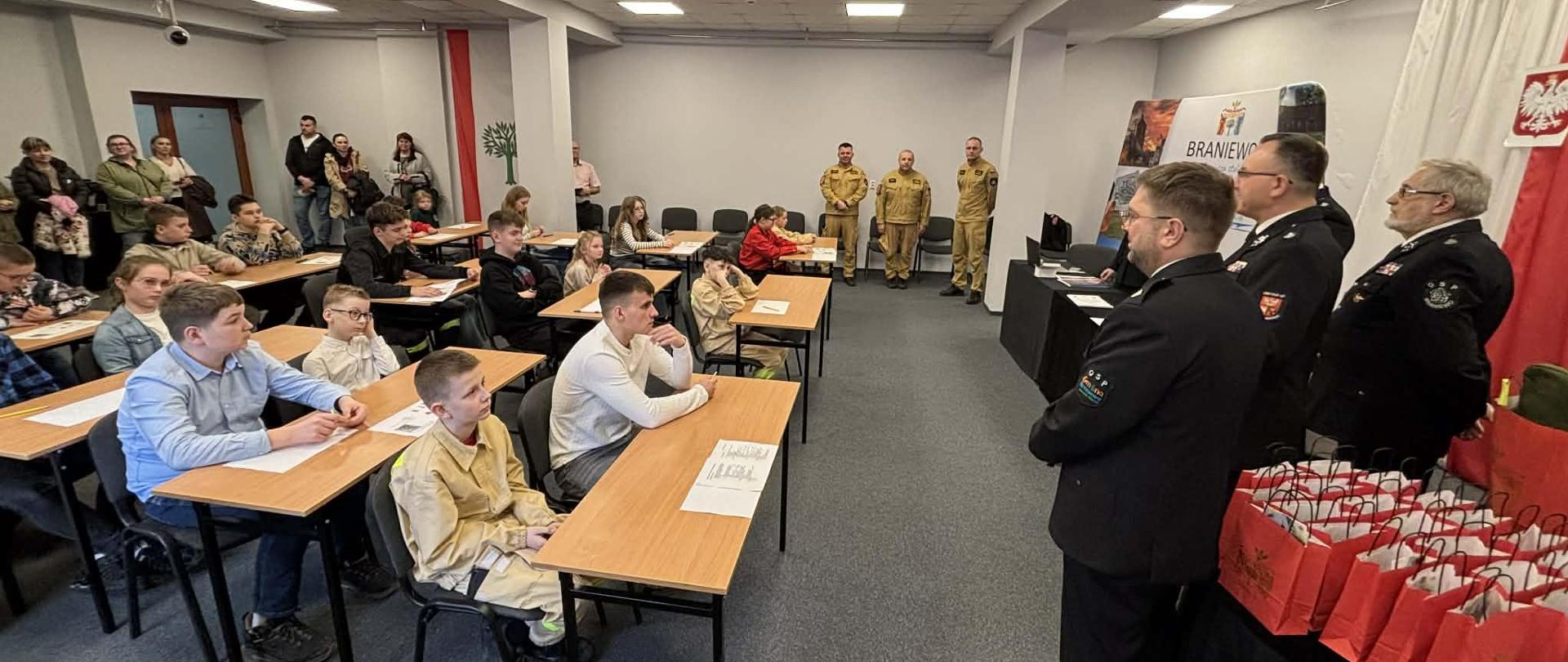 Duża sala. W ławkach z lewej strony siedzą dzieci. Z prawej i na wprost organizatorzy konkursu. Za chwile rozpocznie się turniej wiedzy pożarniczej.