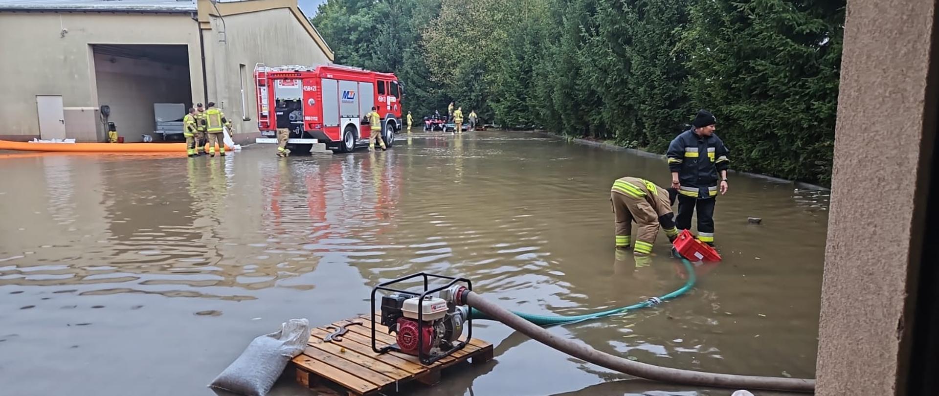 Zalany wodą powodziową teren jednostki KP PSP Kamienna Góra. Na zdjęciu funkcjonariusze w trakcie pompowania wody i budowania zabezpieczeń przed napływającą wodą.
