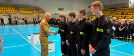 Podczas II Halowych Młodzieżowych Zawodów Sportowo-Pożarniczych na hali sportowej wręczane są medale młodym uczestnikom ubranym w stroje drużynowe.
