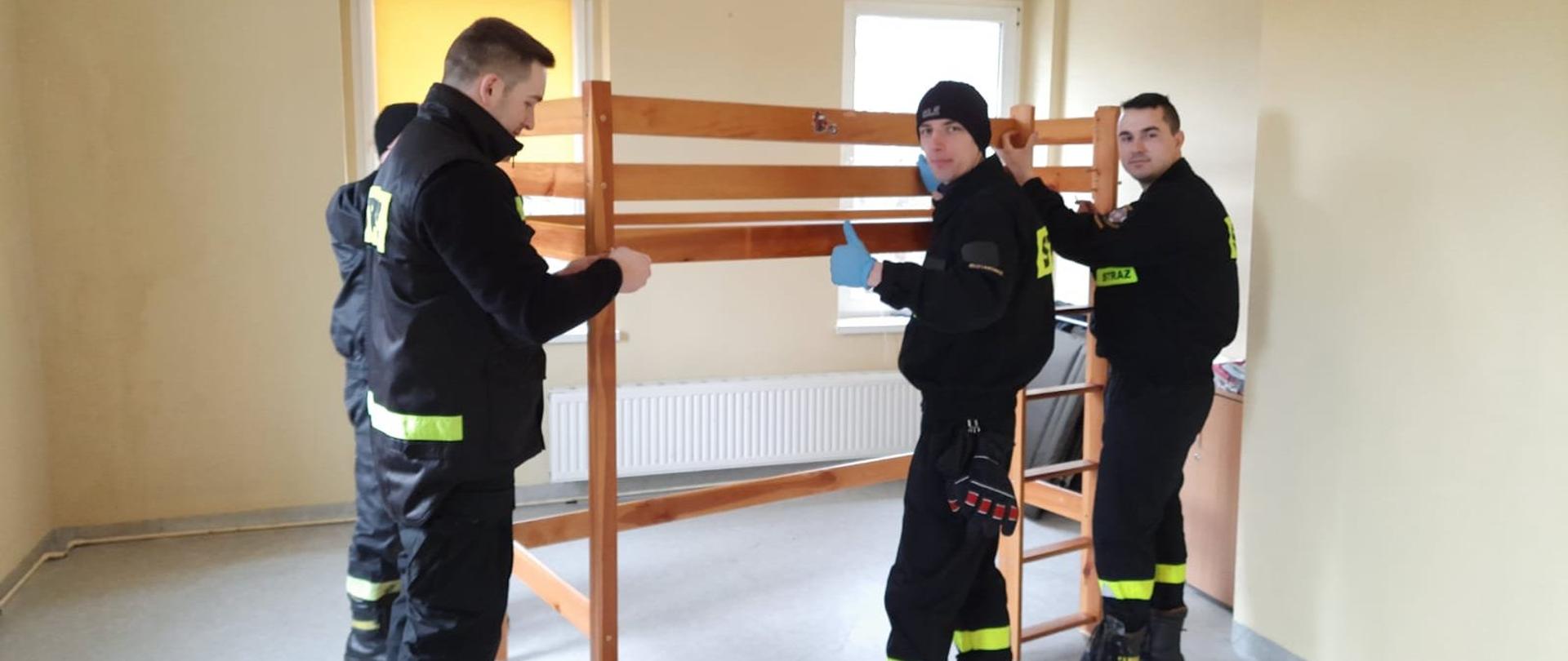 na zdjęciu widać czterech strażaków ochotników, którzy skręcają łóżko. Szykują miejsce do którego przyjadż uchodźcy z Ukrainy.